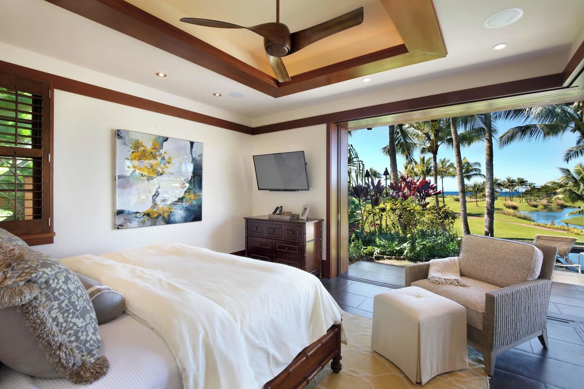 Ein Schlafzimmer mit Bett, Kommode, Fernseher und Blick auf einen Golfplatz.
