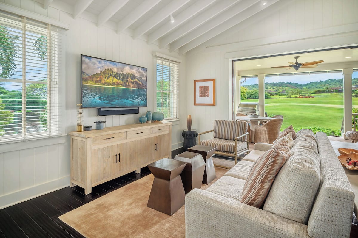 Ein Wohnzimmer mit großem Fernseher, Holzschrank, beiger Couch und Blick auf einen Golfplatz.