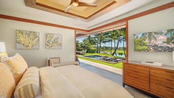 A bedroom with a large bed, a wooden dresser, and a view of a tropical landscape.
