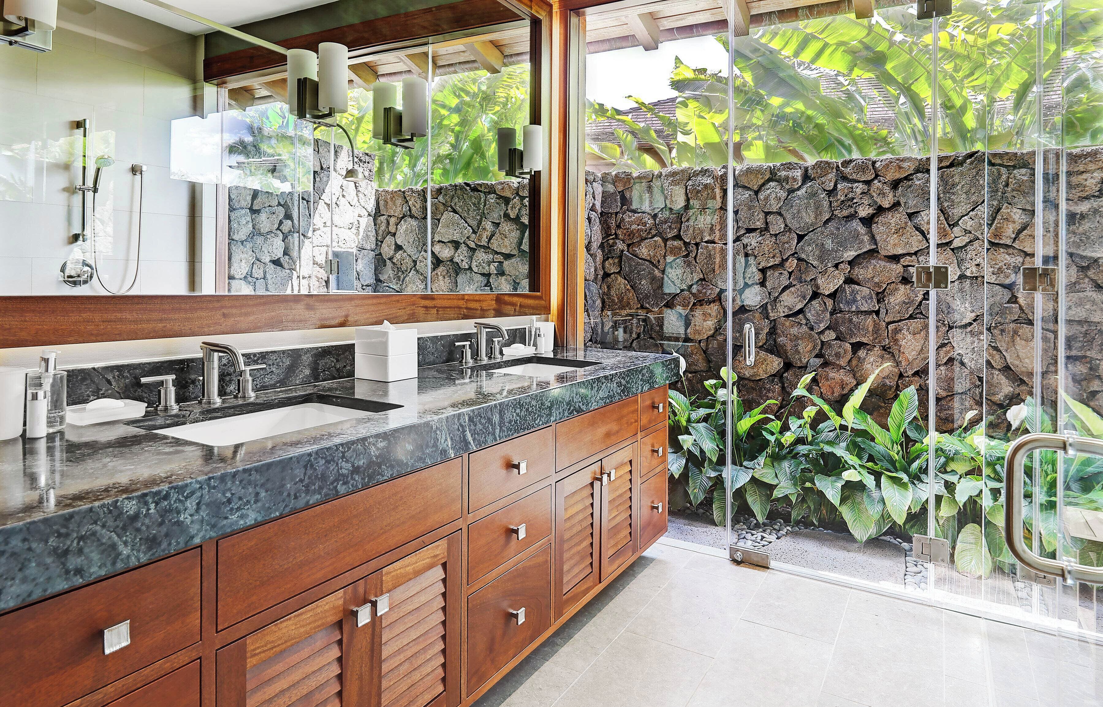 Un baño moderno con un espejo grande, lavamanos dobles y una pared decorativa de piedra.