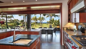 A modern kitchen with a large island, stainless steel appliances, and a view of a golf course and palm trees.