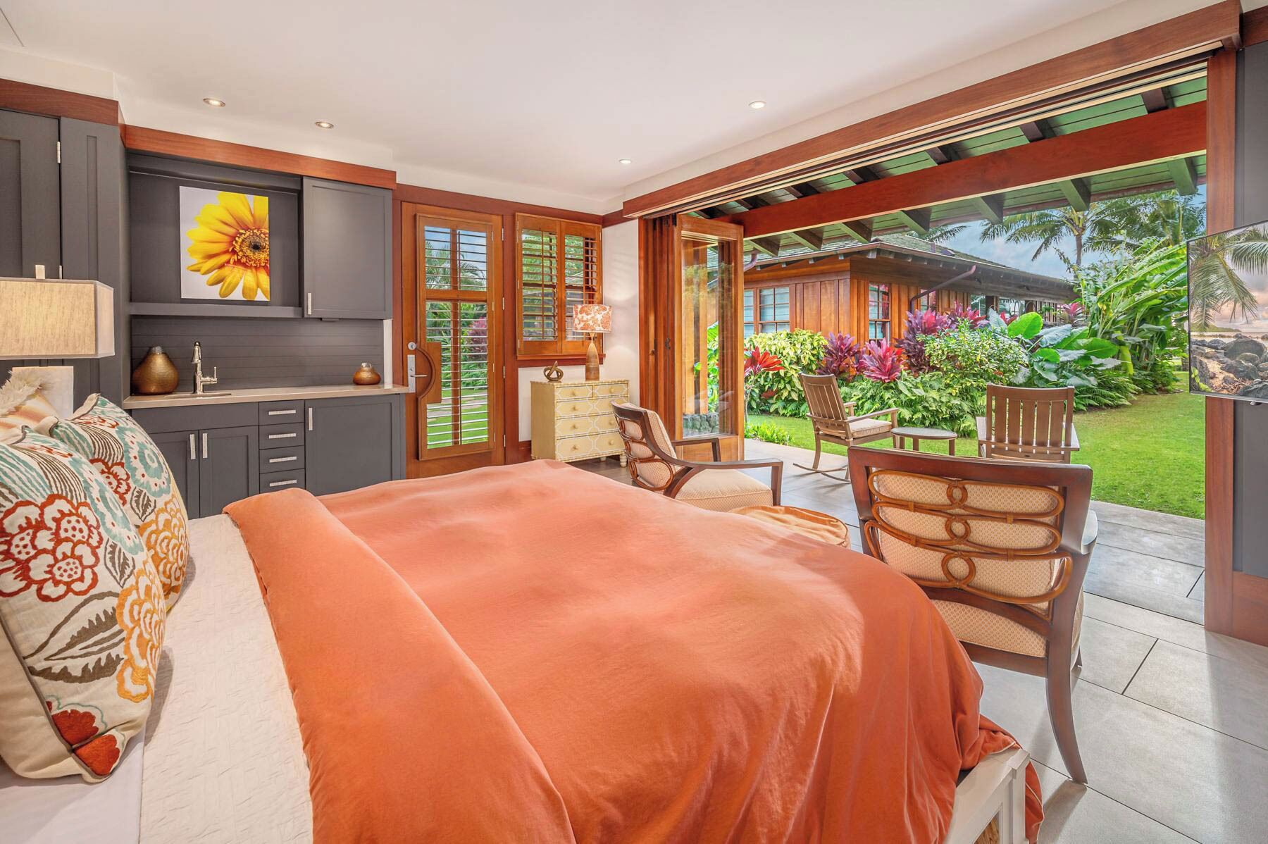 Un dormitorio con una cama grande, una zona de estar con sillones, una cocina y vistas a un jardín.