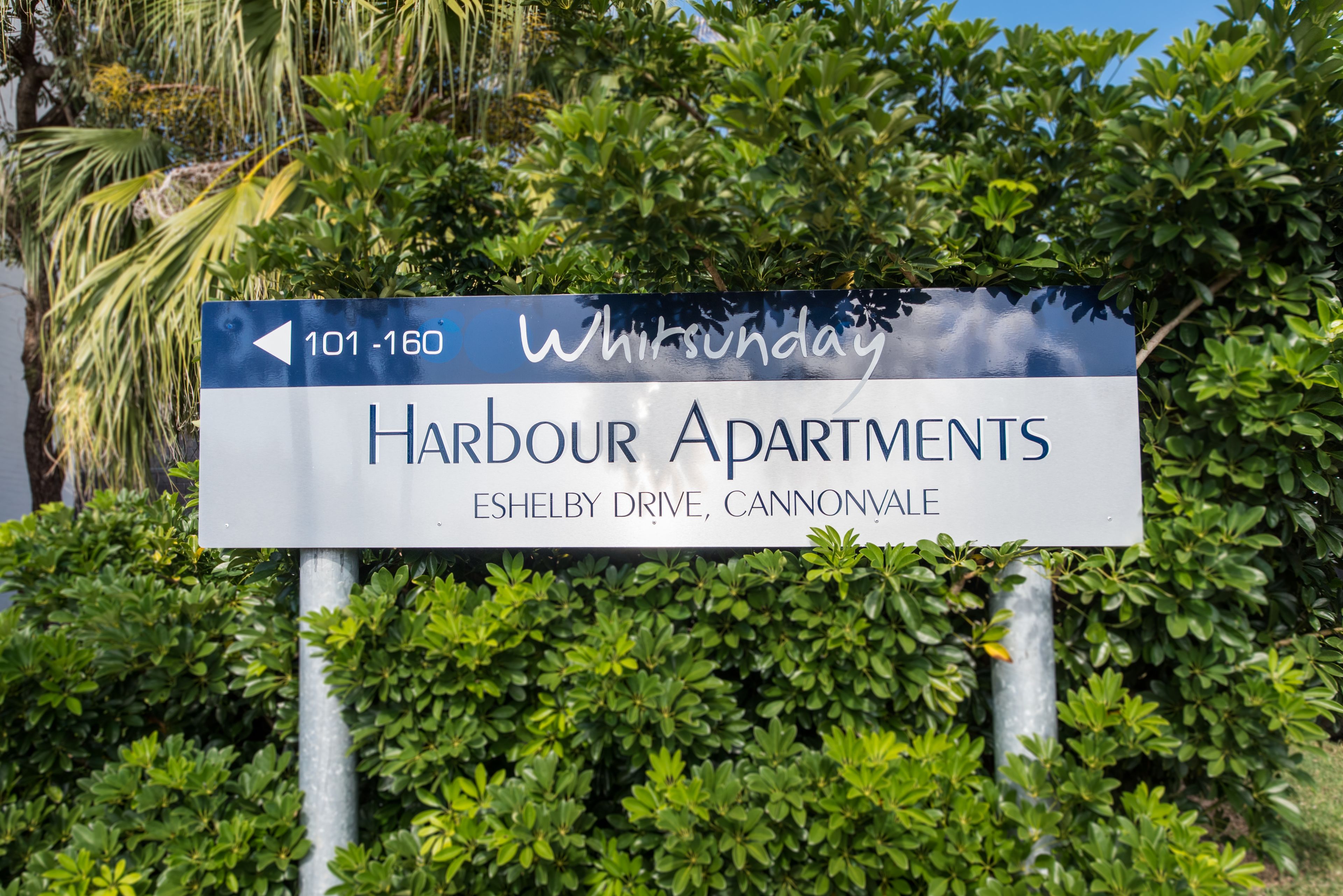 A sign for Harbour Apartments with directional arrows and the address Eshelby Drive, Cannonvale.