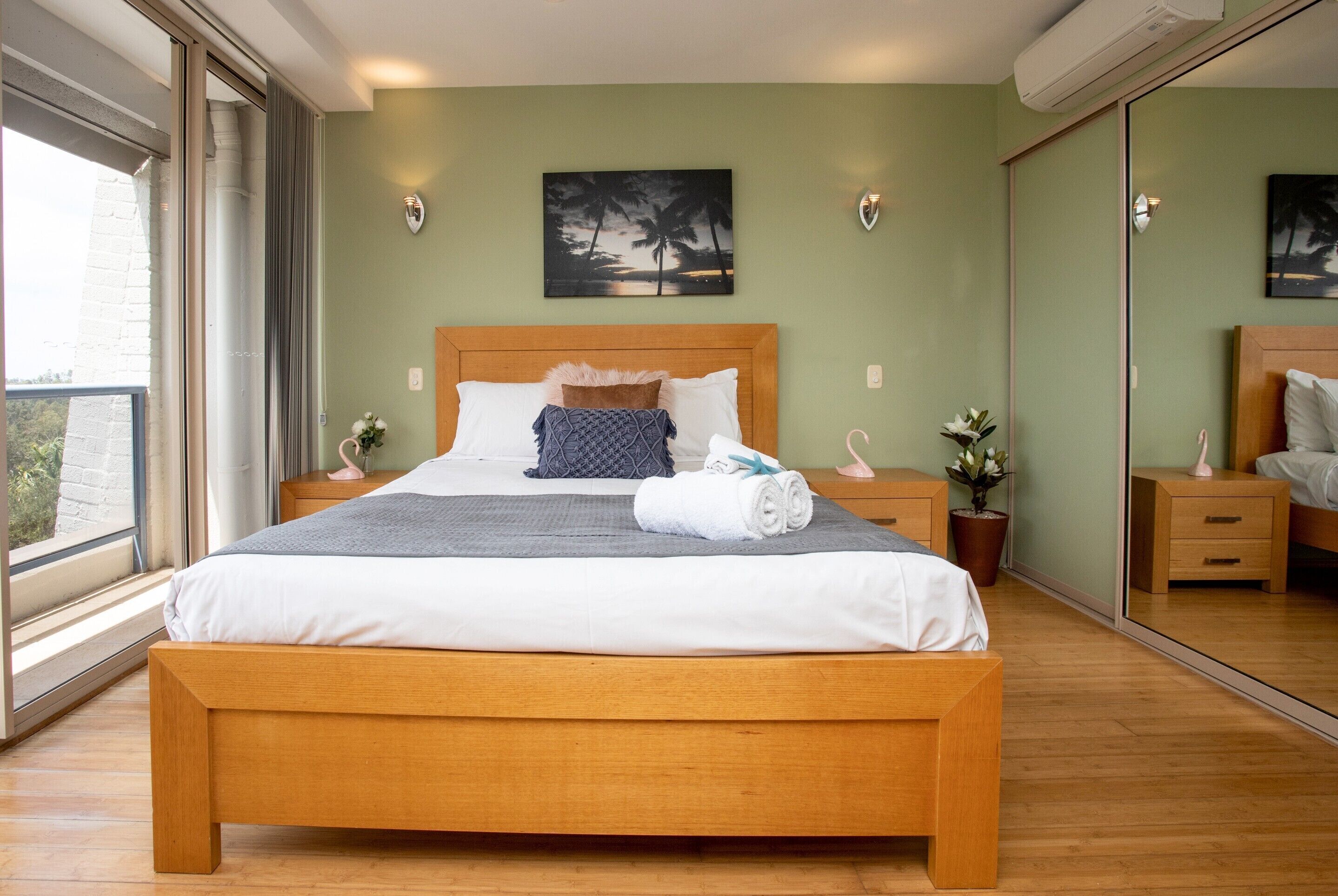 Un dormitorio con una cama grande, una mesita de noche, una planta en maceta y un espejo amplio.