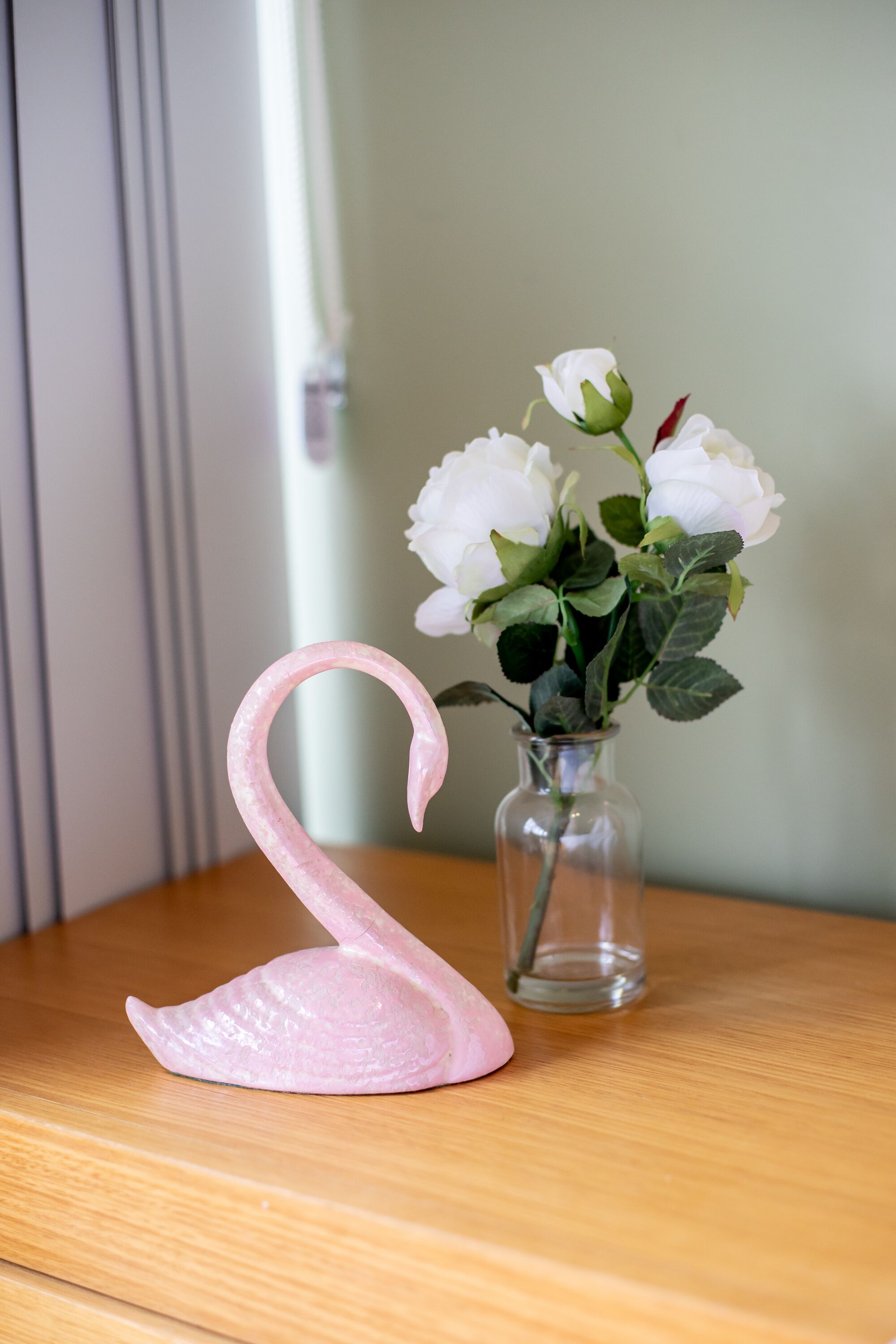 A pink swan figurine next to a vase with white flowers on a wooden surface.
