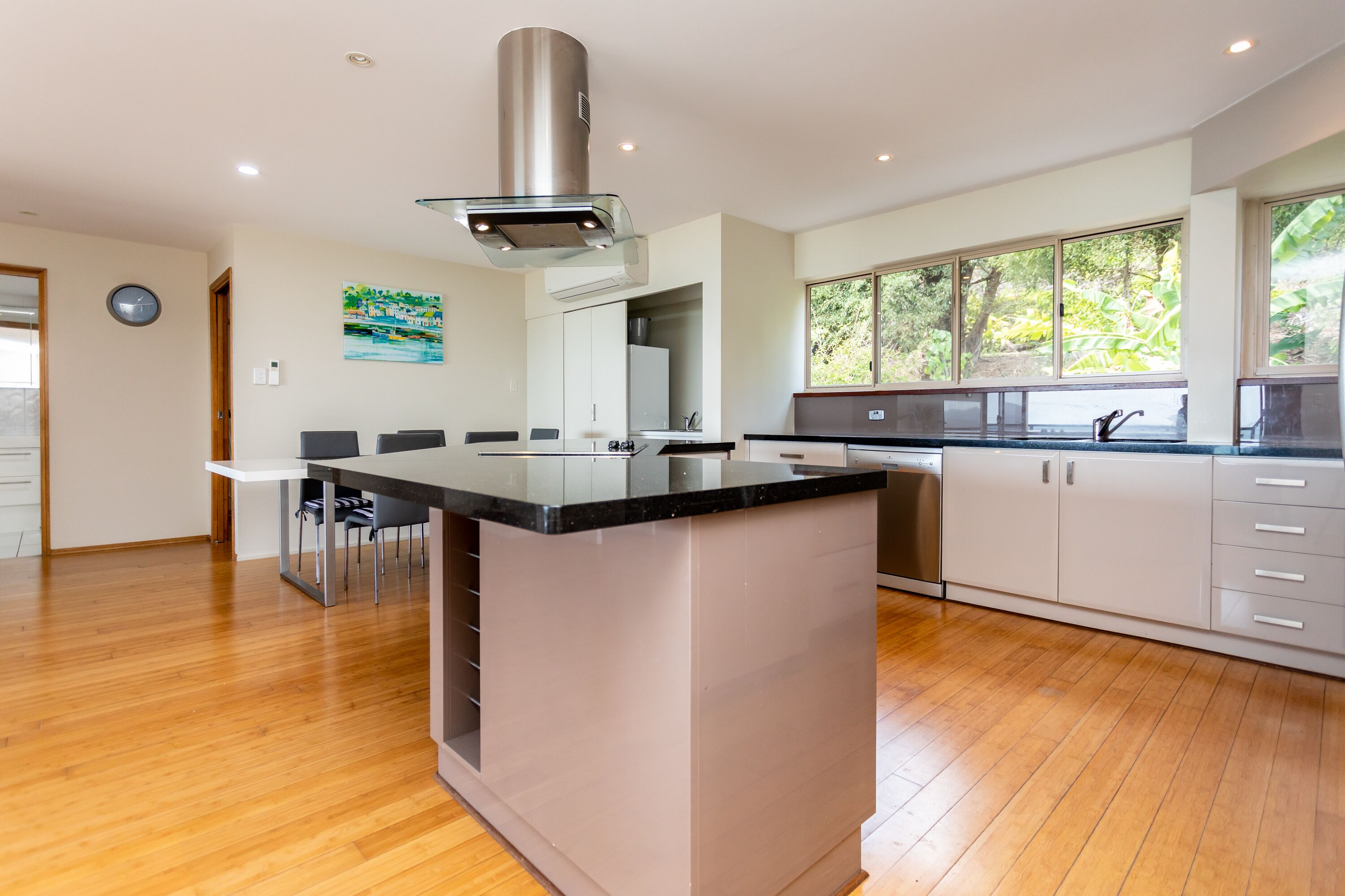 A modern kitchen with a central island, white cabinetry, and a large window providing natural light.