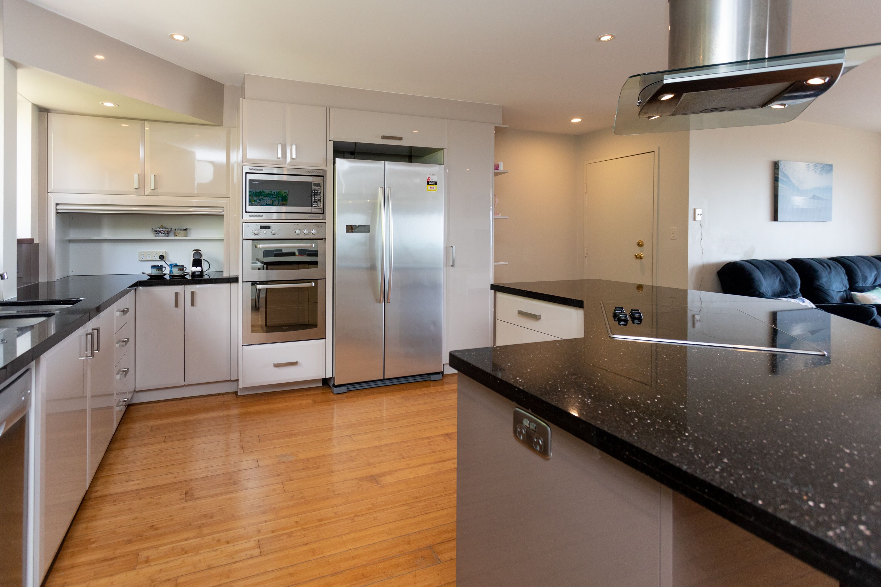 A modern kitchen with stainless steel appliances, wooden flooring, and a black granite countertop.