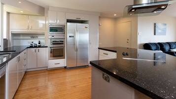 A modern kitchen with stainless steel appliances, wooden flooring, and a black granite countertop.