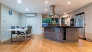 A modern kitchen with a central island, built-in appliances, and a dining area with chairs. - Getaway Ocean Views (Cannonvale)