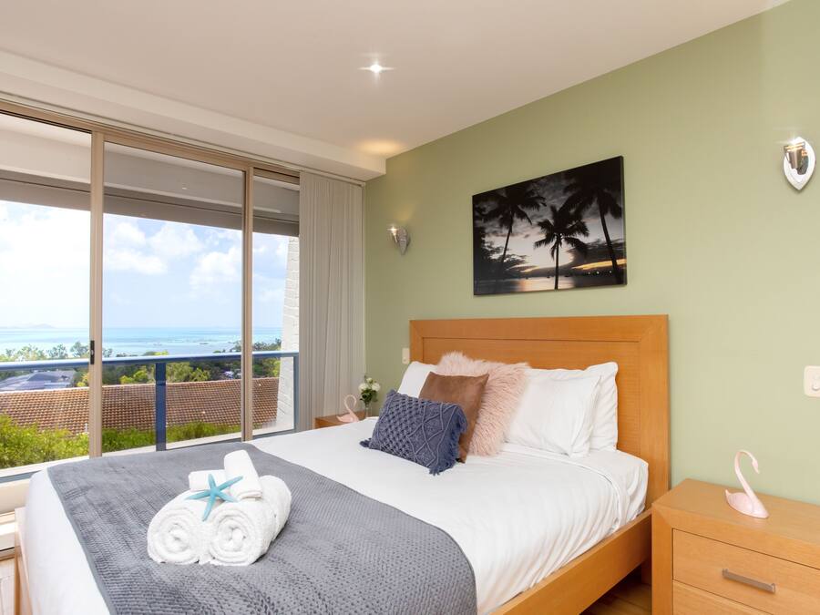 A hotel room with a large bed, a view of the sea, and a painting of palm trees.
