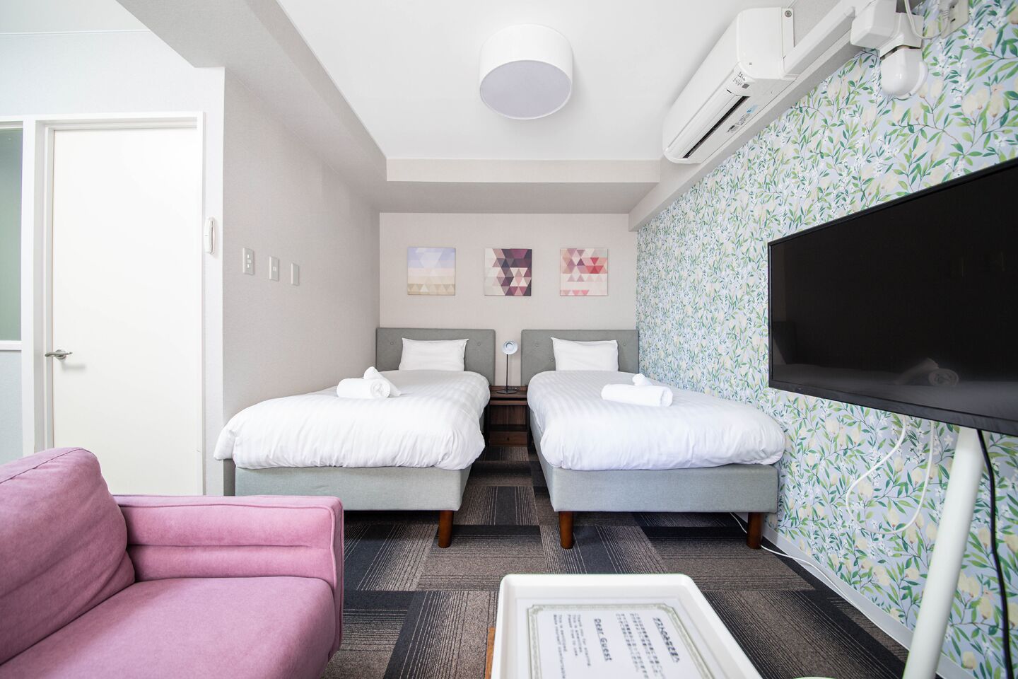 A hotel room with two beds, a TV, and a pink couch.