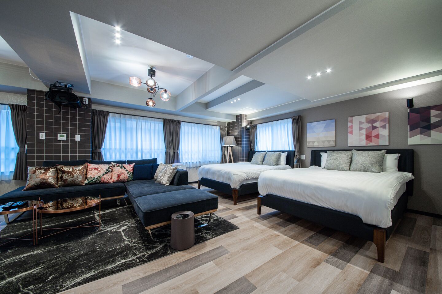 Una habitación de hotel moderna con sofá modular, dos camas individuales, un escritorio y un amplio ventanal con cortinas.