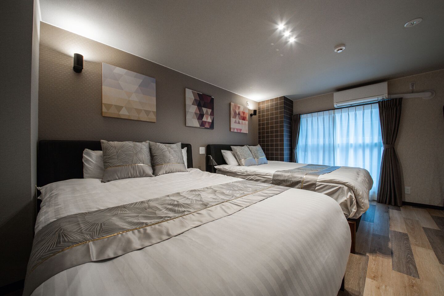 Una habitación de hotel con dos camas, un ventanal con cortinas y obras de arte en las paredes.