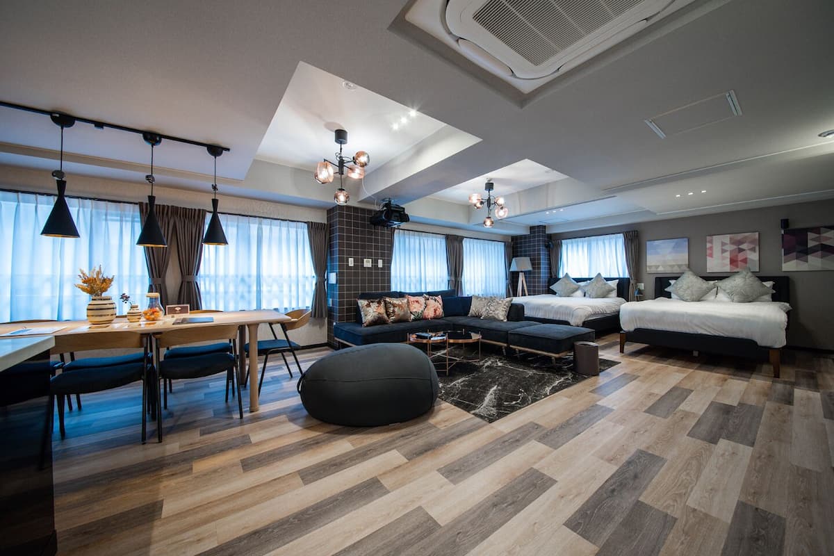 Quarto de hotel moderno com área de jantar, sofá, cama e uma janela grande.