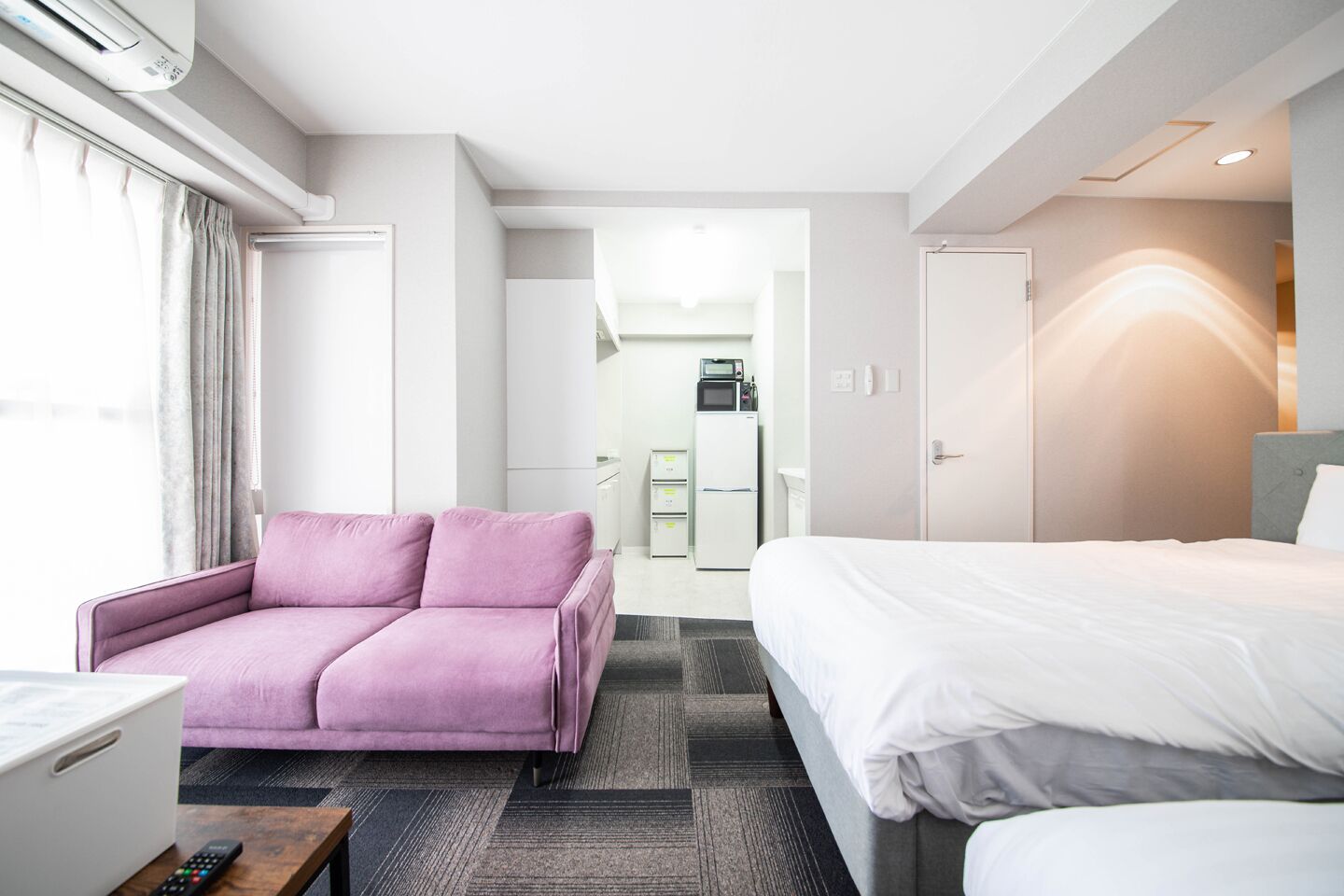Ein Hotelzimmer mit Bett, einer Couch, einem Schreibtisch mit Computer und einer kleinen Küche im Hintergrund.