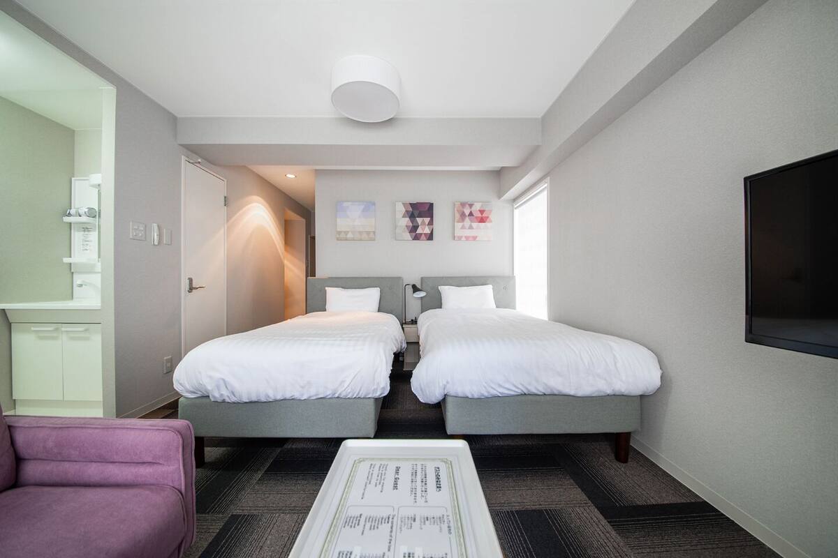 Quarto de hotel com duas camas, uma escrivaninha, uma cadeira e uma televisão.