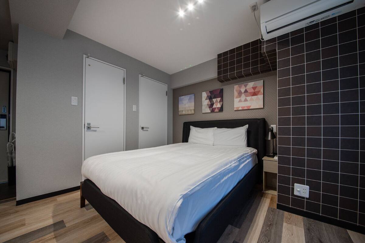 Quarto com cama, mesa de cabeceira, ar condicionado fixado na parede e porta.