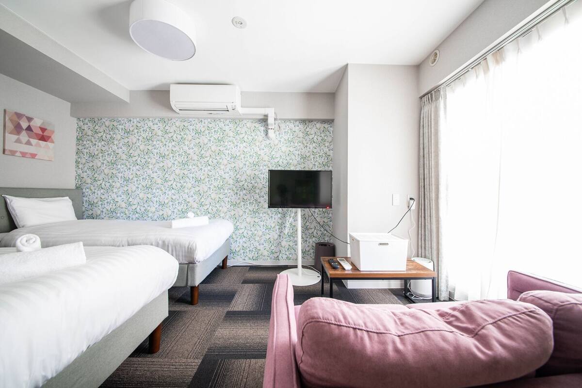 Quarto de hotel com duas camas, televisão, escrivaninha com abajur e janela com cortinas.