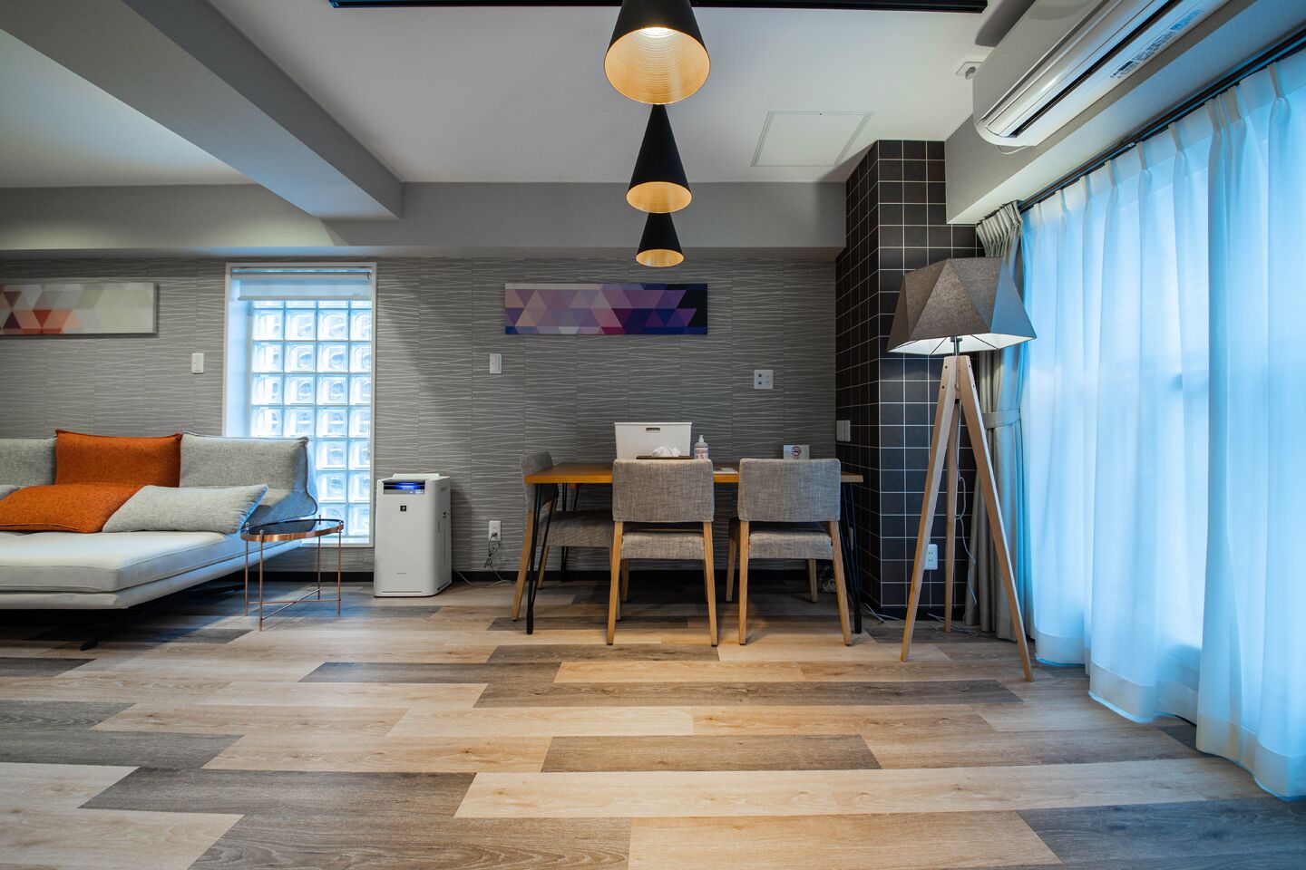 Un salon moderne comprenant un canapé, une table à manger avec des chaises, un lampadaire et une grande fenêtre avec des stores.