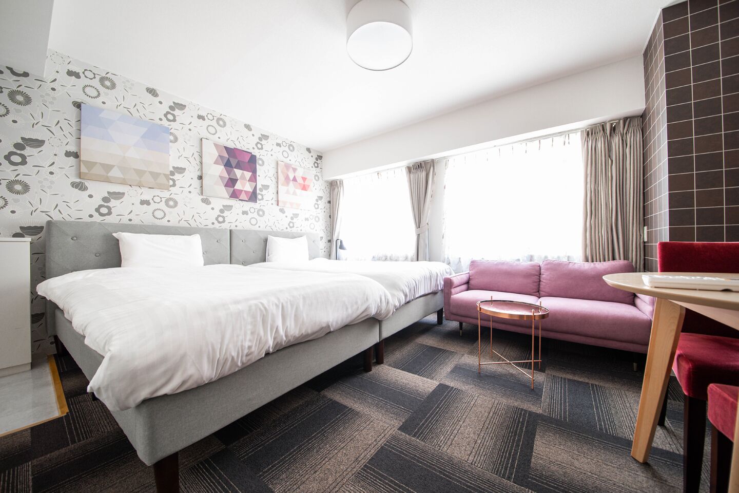 A hotel room with a bed, a sofa, a small table, and a window with curtains.