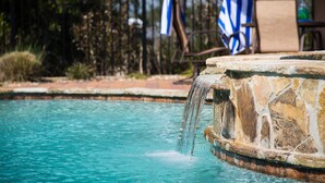 A pool with a stone waterfall feature, surrounded by a fence and chairs with blue and white towels. - Your Own Private Waterfront Resort! Pool, Hot Tub, Lagoon, Kayaks, Bikes & More! (Gulf Shores)