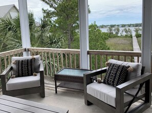 Une terrasse extérieure couverte, dotée de deux fauteuils confortables, d’une petite table et offrant une vue sur une étendue d’eau et la verdure environnante.