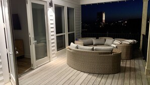 A covered outdoor deck with wicker furniture and a glass door leading to a room. - Your Own Private Waterfront Resort! Pool, Hot Tub, Lagoon, Kayaks, Bikes & More! (Gulf Shores)