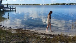 A person walking along a lakeshore with a dock and houses in the background. - Your Own Private Waterfront Resort! Pool, Hot Tub, Lagoon, Kayaks, Bikes & More! (Gulf Shores)
