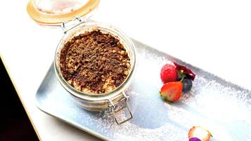 Un dessert servi dans un bocal en verre muni d’un couvercle métallique à fermoir, accompagné de fraises et de framboises présentées sur un plateau en argent.