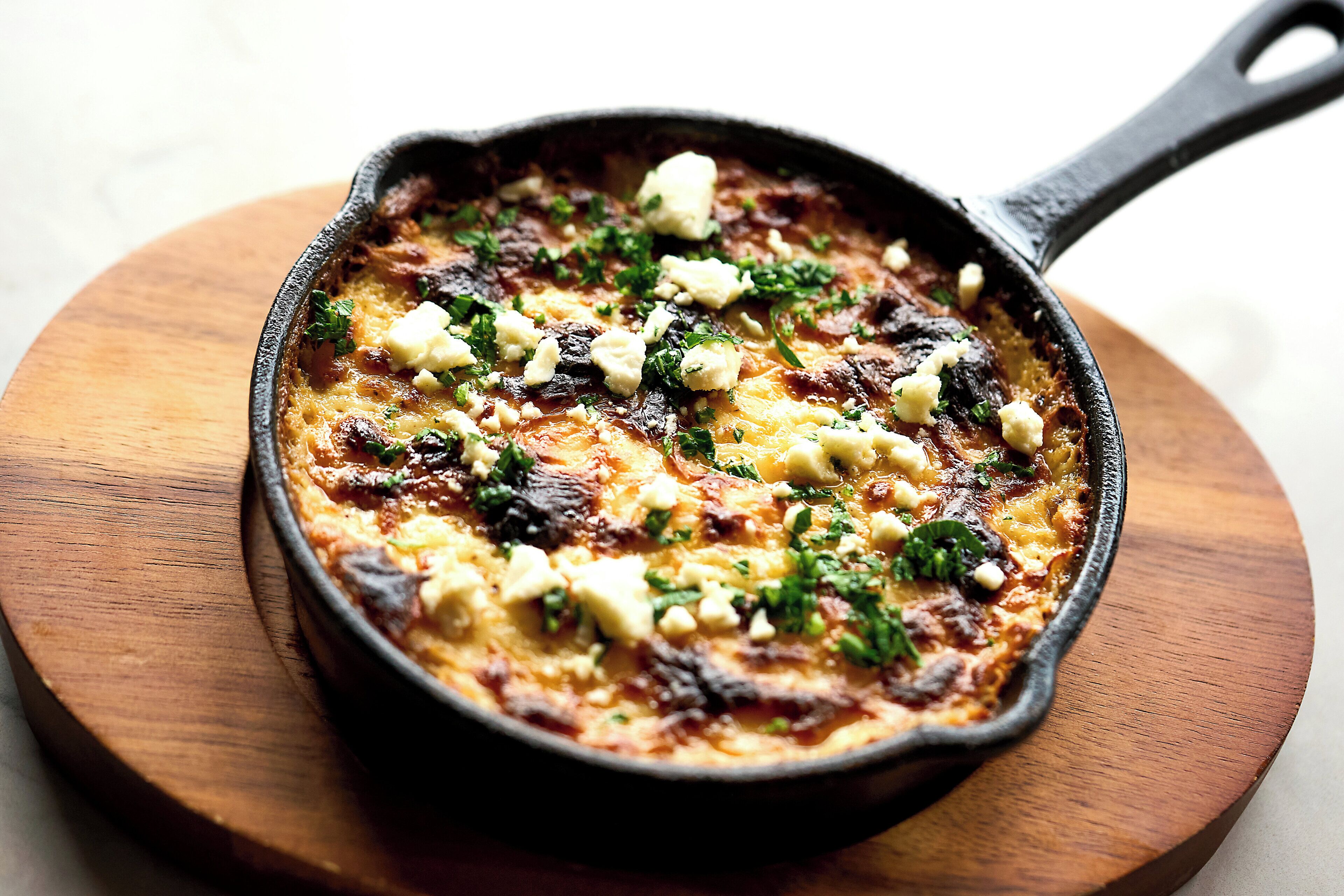 A skillet with a dish on a wooden board.