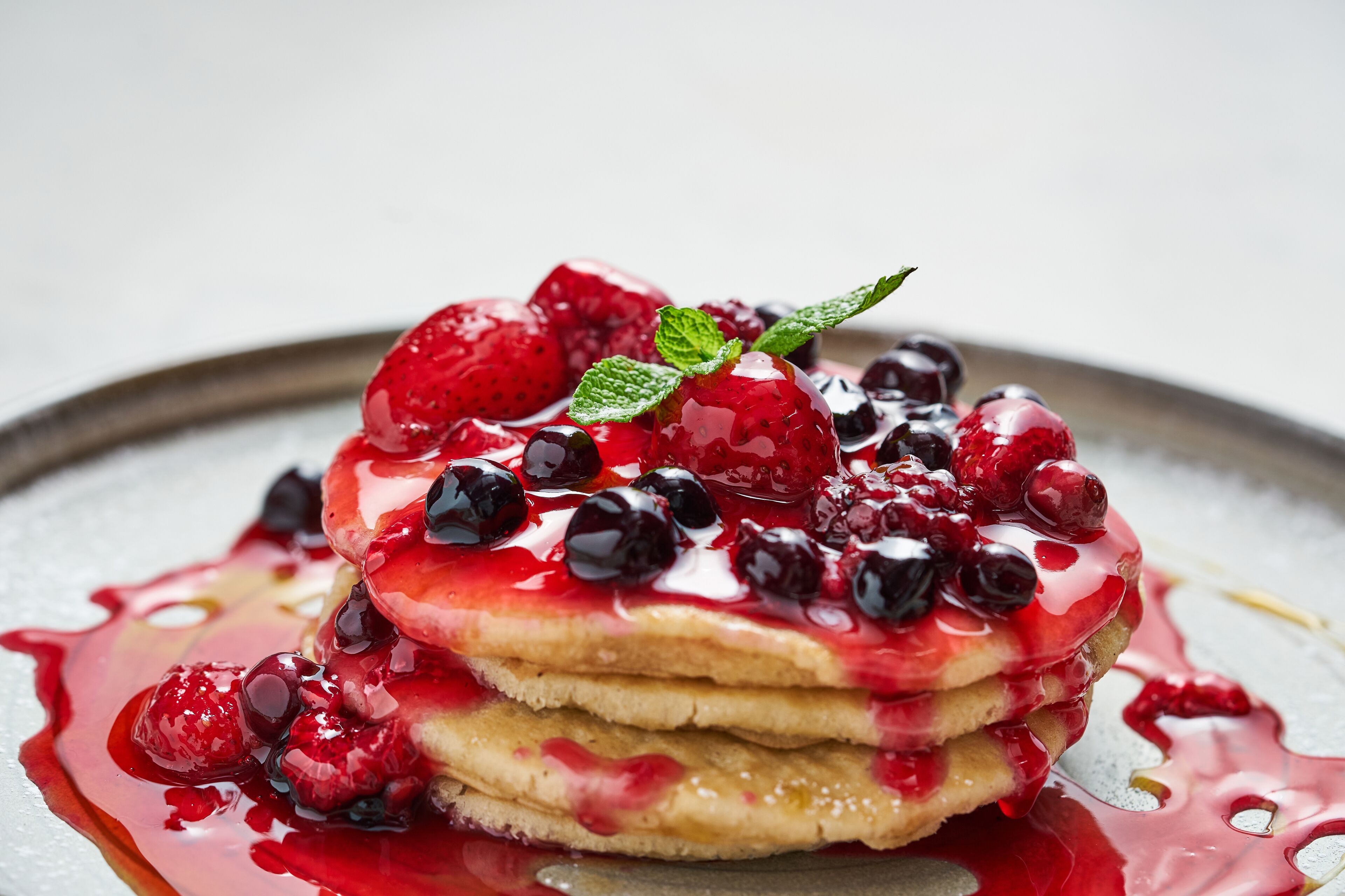 Une pile de crêpes garnie de fruits rouges et nappée de sirop.