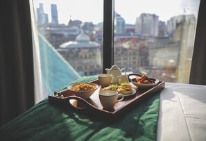 A breakfast tray with various dishes on a bed with a green bedspread, overlooking a cityscape through a window. - Hotel Indigo Manchester - Victoria Station by IHG (Manchester)