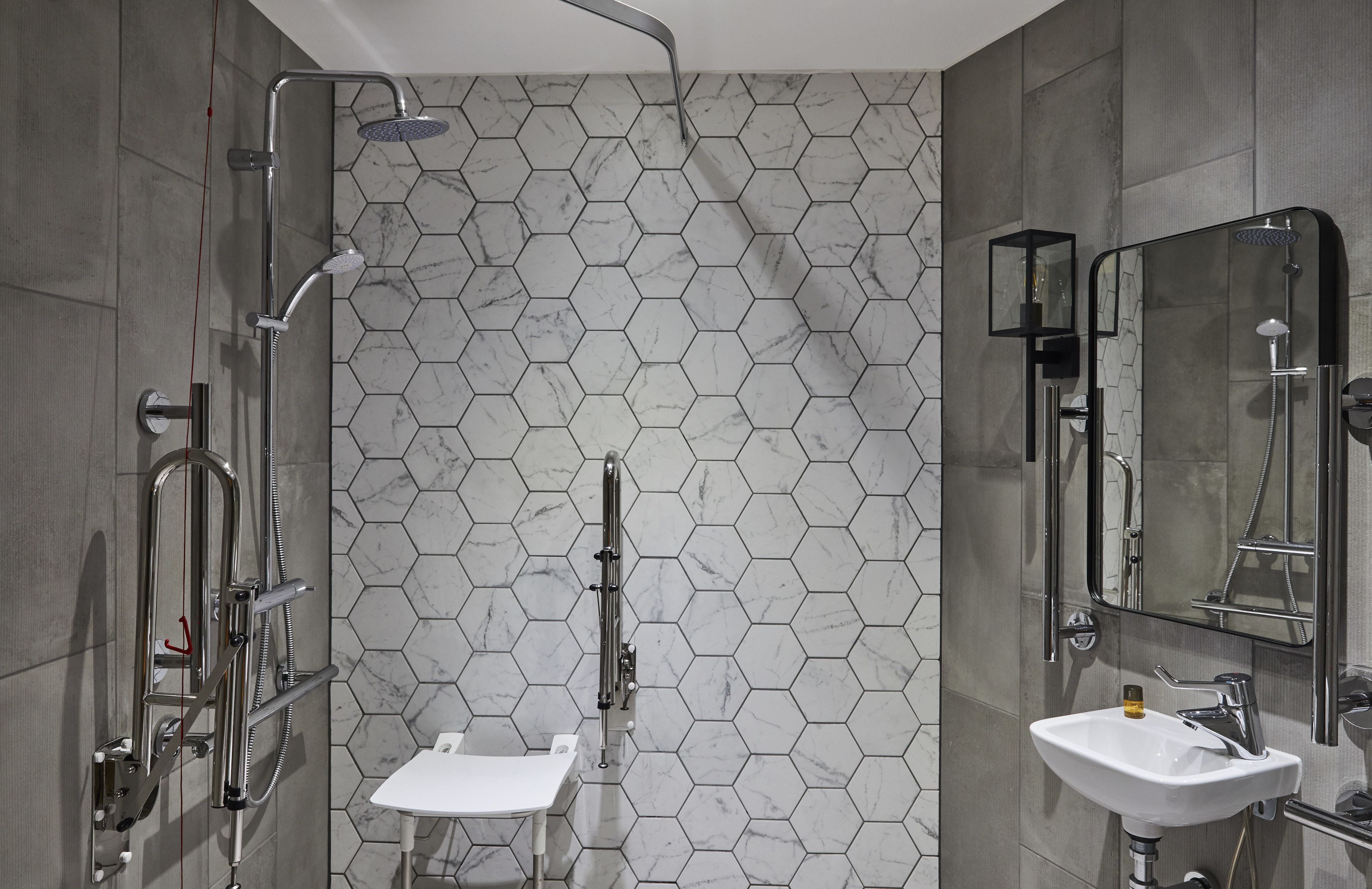 A modern bathroom with a hexagonal tile backsplash, a shower with a handheld showerhead, a sink with a mirror, and a toilet.