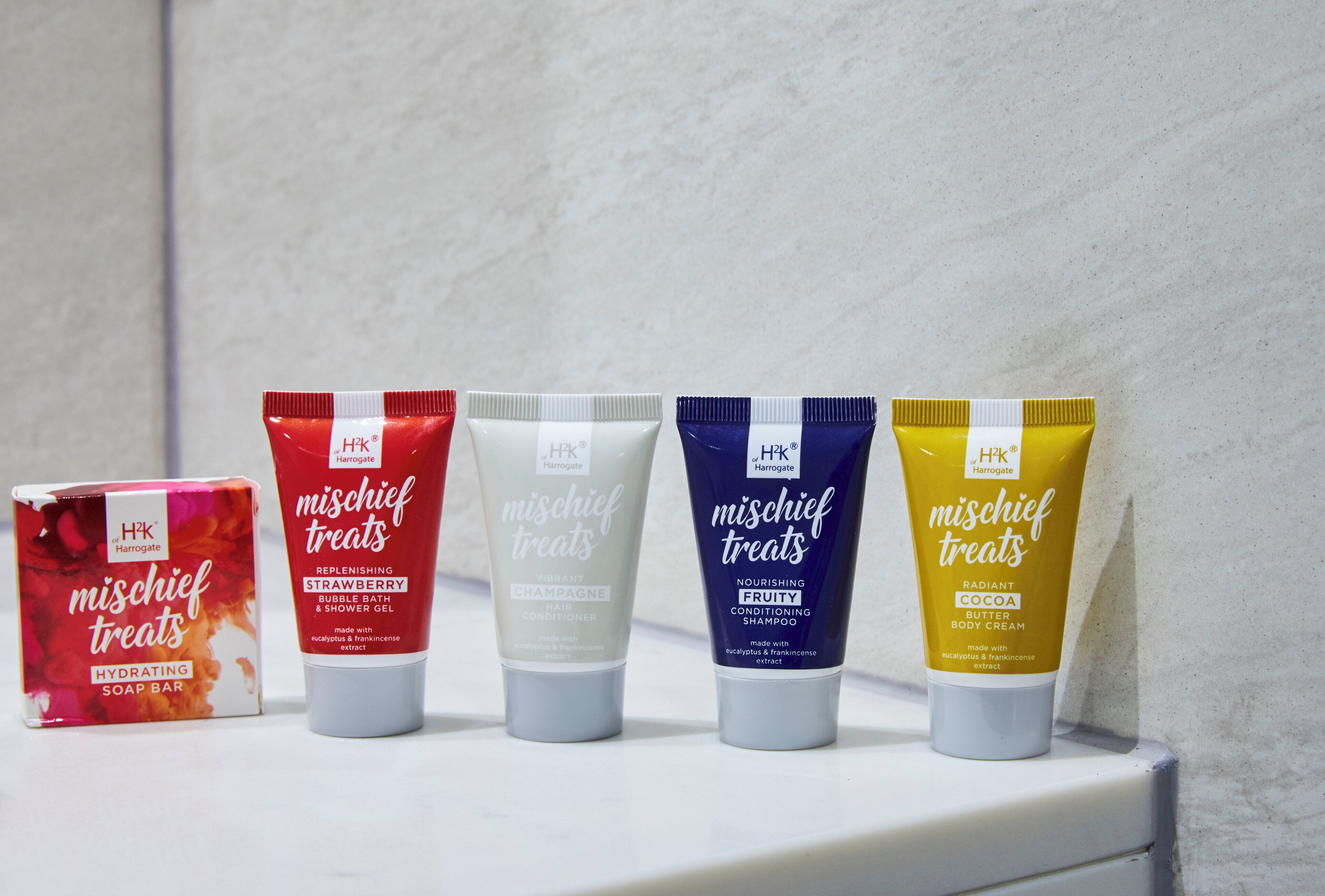 Four tubes of H2K Harrogate Mischief Treats on a white shelf against a plain wall.