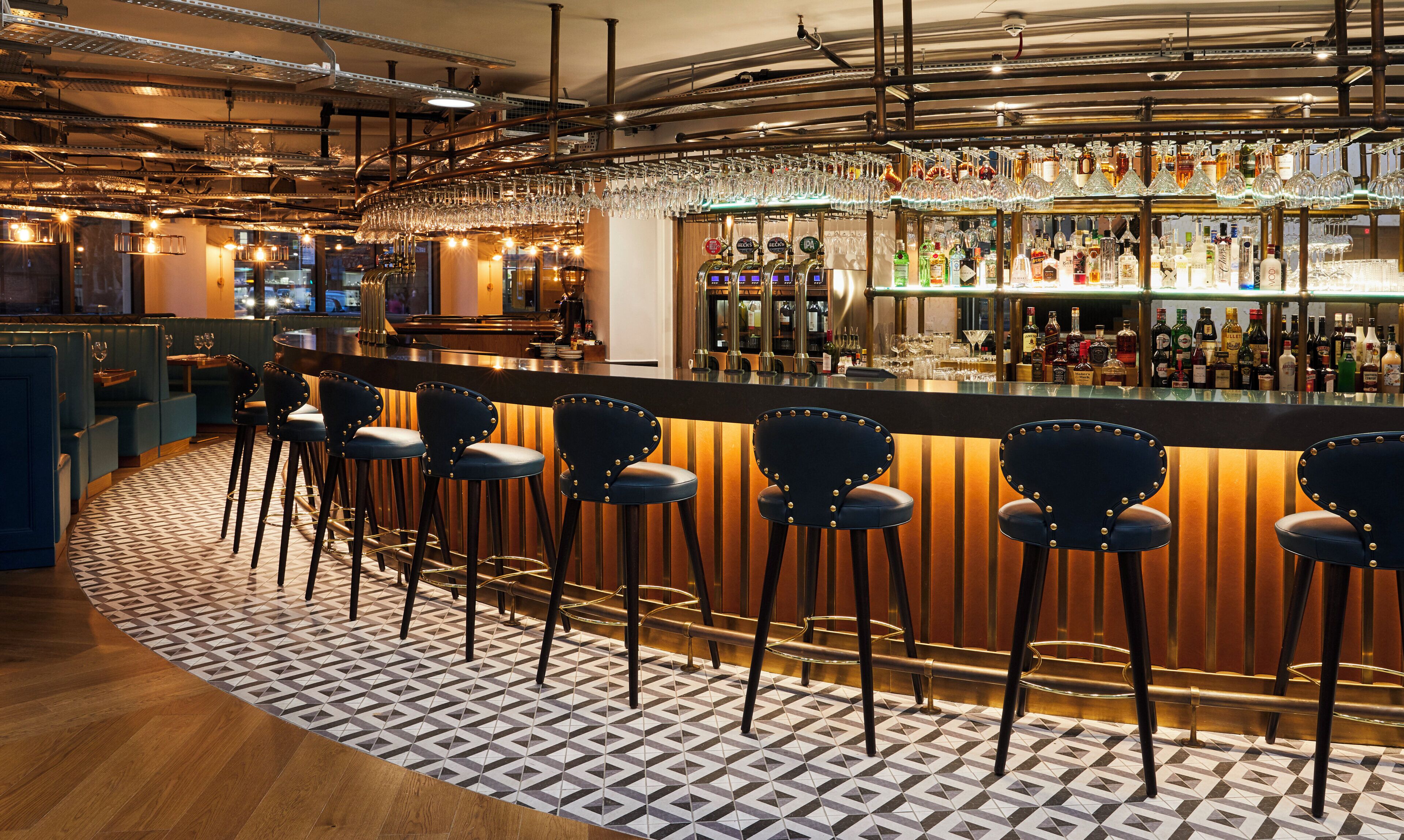 A bar area with stools, a bar counter, and a variety of bottles and glasses.