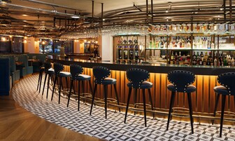 A bar area with stools, a bar counter, and a variety of bottles and glasses.