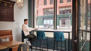 A man working at a desk with a laptop, a window with a view of buildings, and a wooden board with platform numbers. - Hotel Indigo Manchester - Victoria Station by IHG (Manchester)