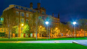 A historic building with multiple chimneys and a large central tower, surrounded by a well-lit courtyard with trees and street lamps. - Hotel Indigo Manchester - Victoria Station by IHG (Manchester)