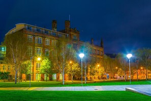 A historic building with multiple chimneys and a large central tower, surrounded by a well-lit courtyard with trees and street lamps. - Hotel Indigo Manchester - Victoria Station by IHG (Manchester)