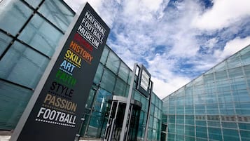 A modern building with a glass facade and a sign listing various themes like football, drama, and art.