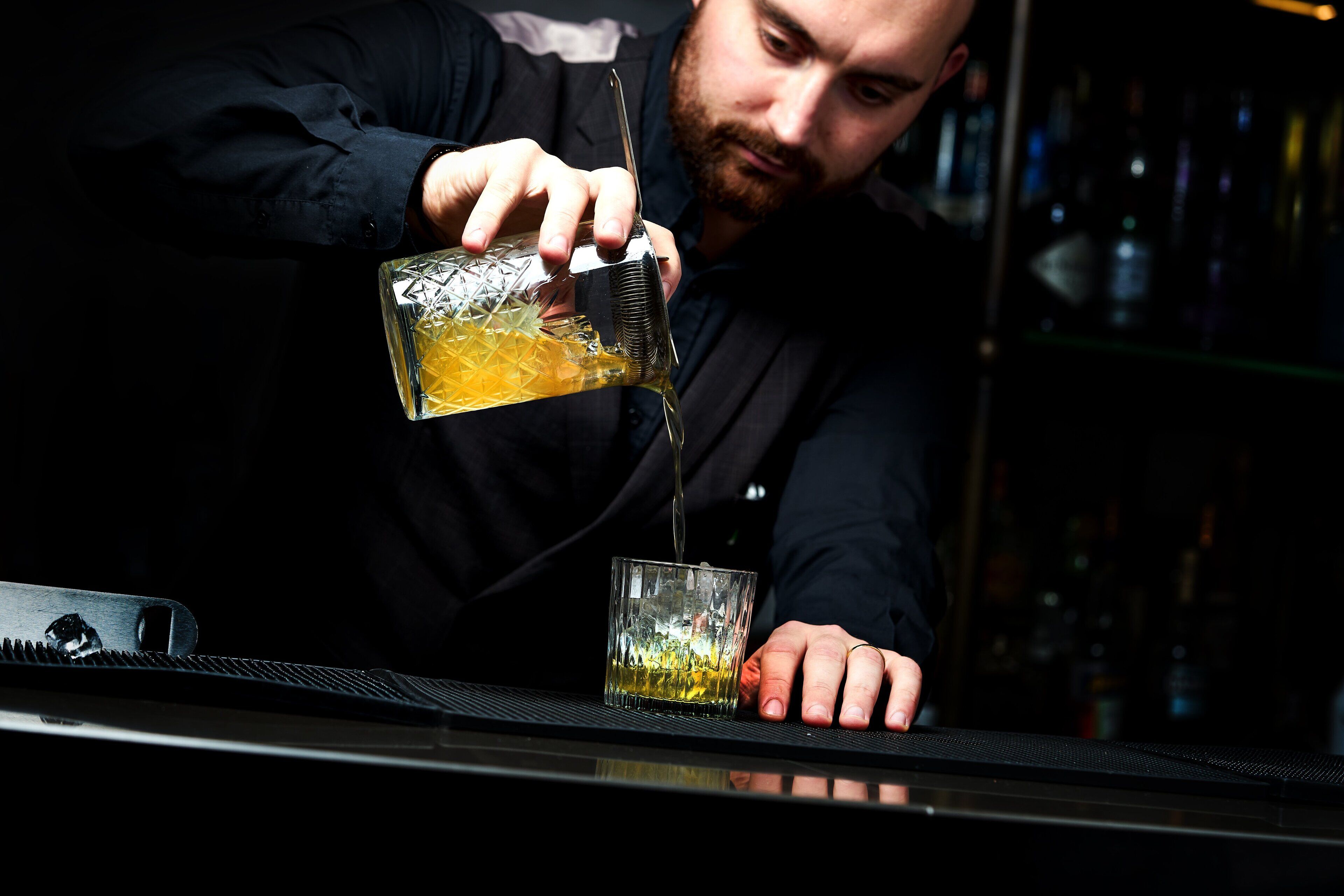A person pouring a drink into a glass on a bar counter.