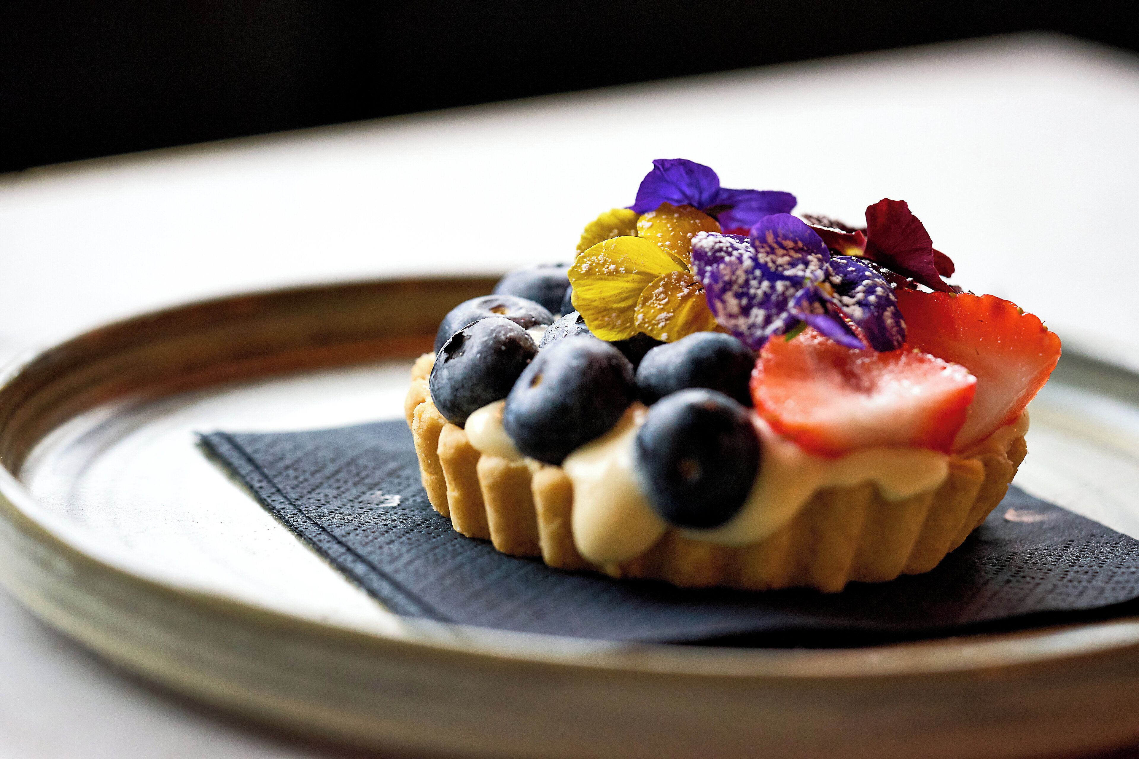 Un postre con arándanos, fresas y flores comestibles sobre un plato.