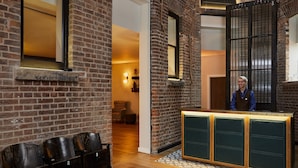 A reception area with a brick wall, a wooden reception desk, and a seating area with numbered chairs. - Hotel Indigo Manchester - Victoria Station by IHG (Manchester)