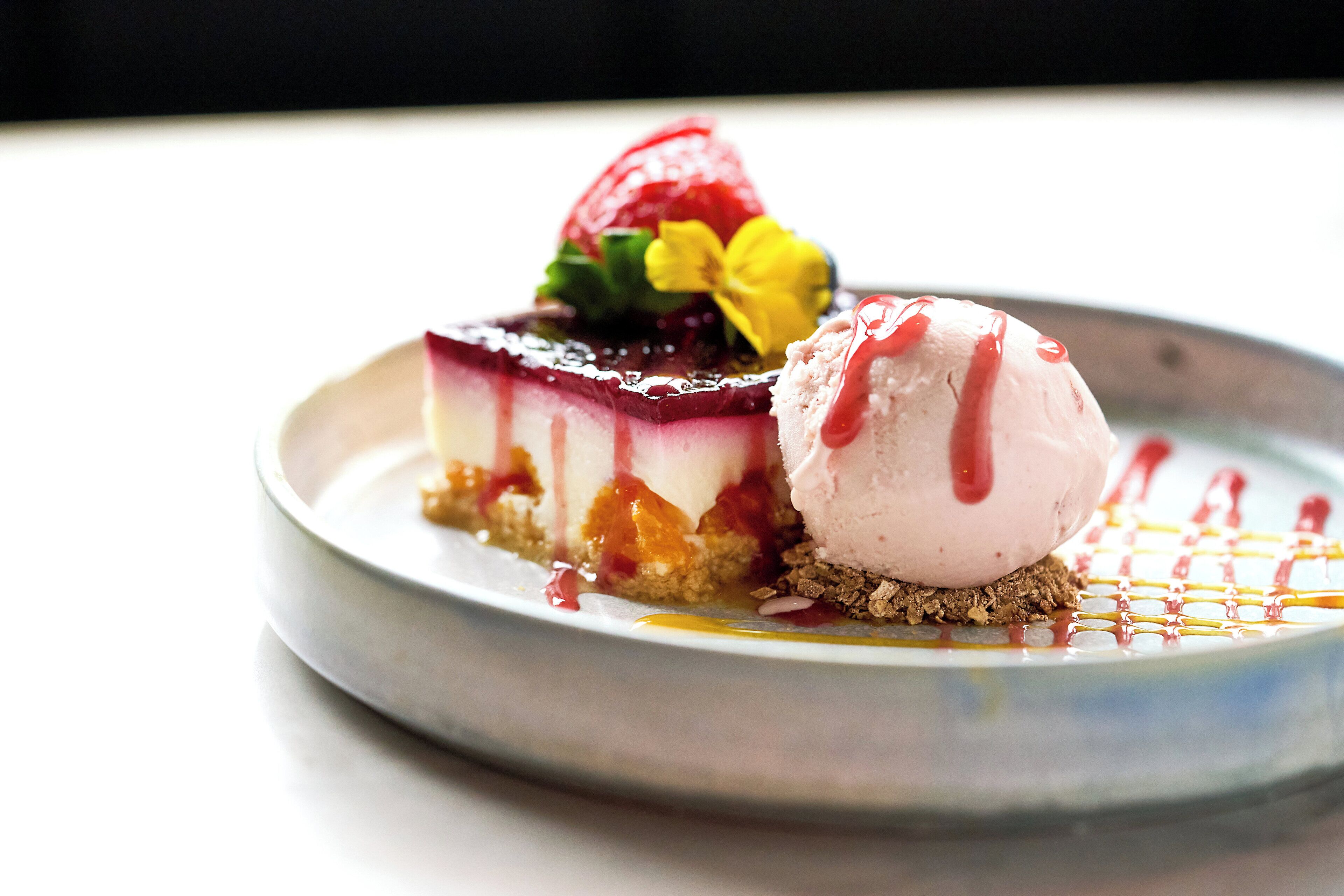 Postre con cobertura de frutos rojos y una bola de helado sobre un plato.