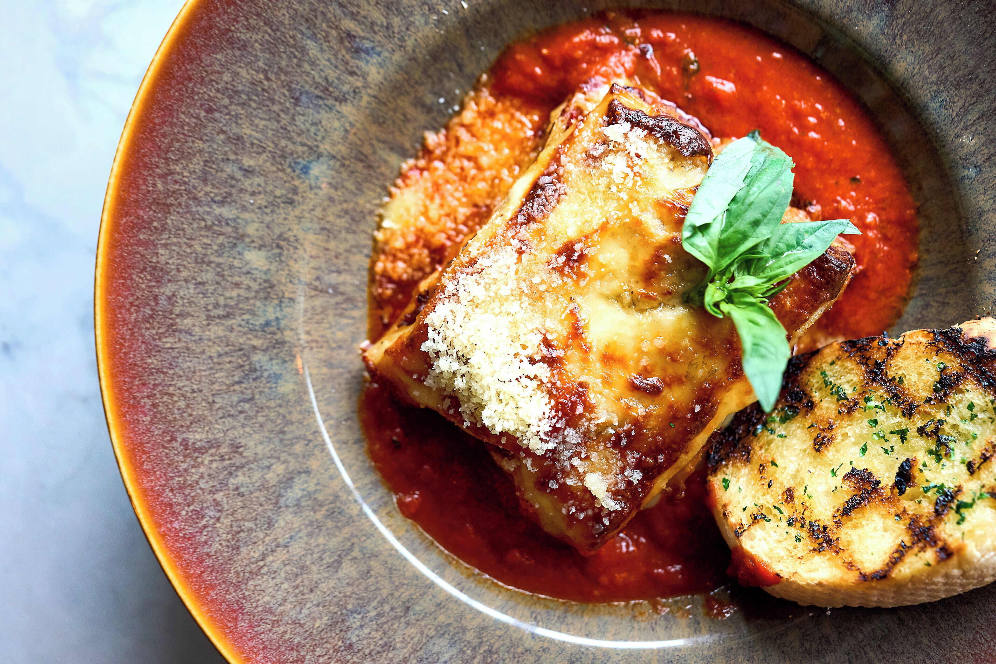 A dish of lasagna with a side of grilled bread, served in a ceramic bowl.