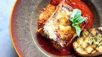 A dish of lasagna with a side of grilled bread, served in a ceramic bowl.