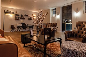 A modern living room with leather sofas, a glass coffee table, and a vase with flowers. - Hotel Indigo Manchester - Victoria Station by IHG (Manchester)