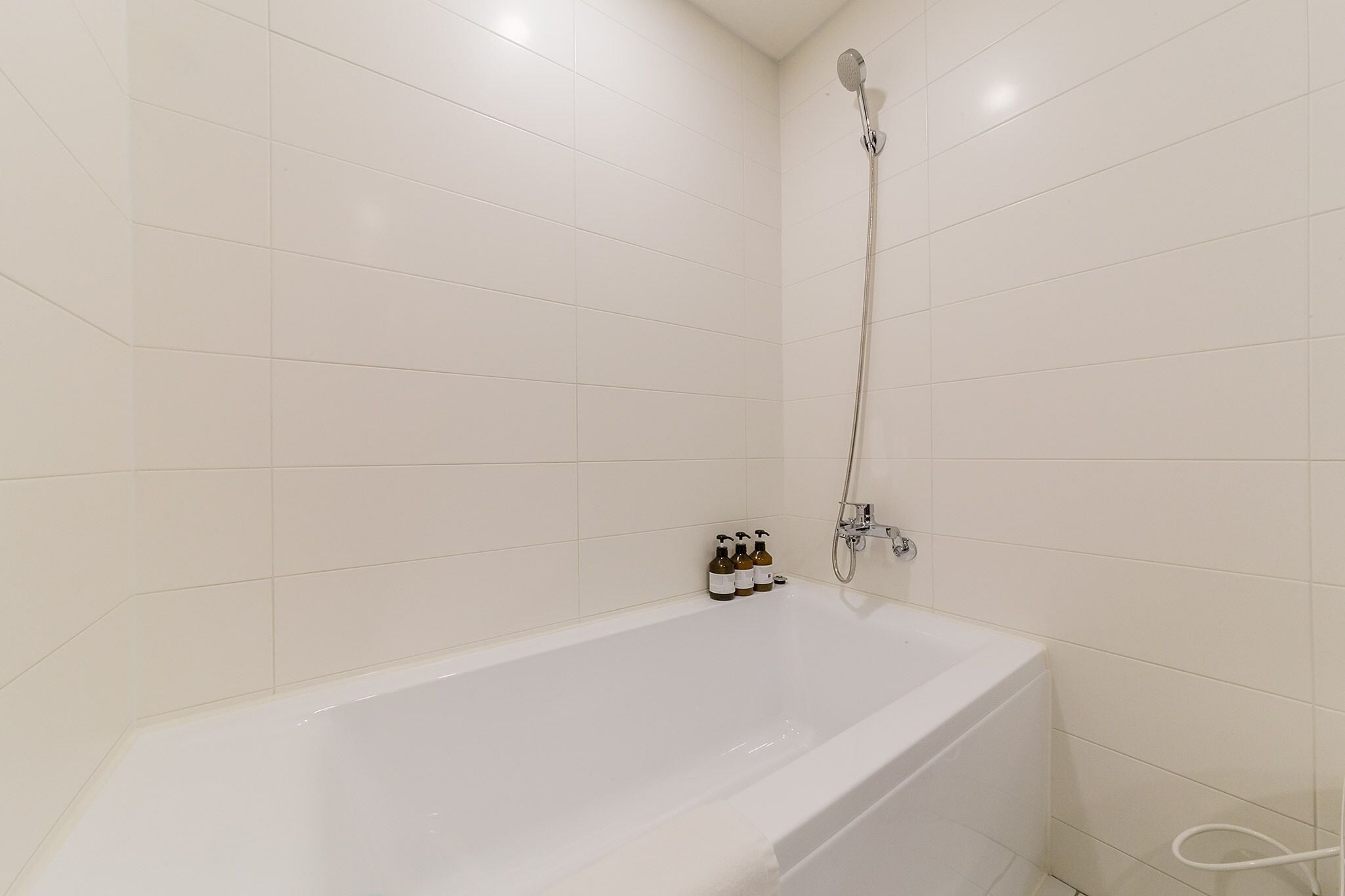 A white bathtub with a showerhead and two bottles of shampoo.