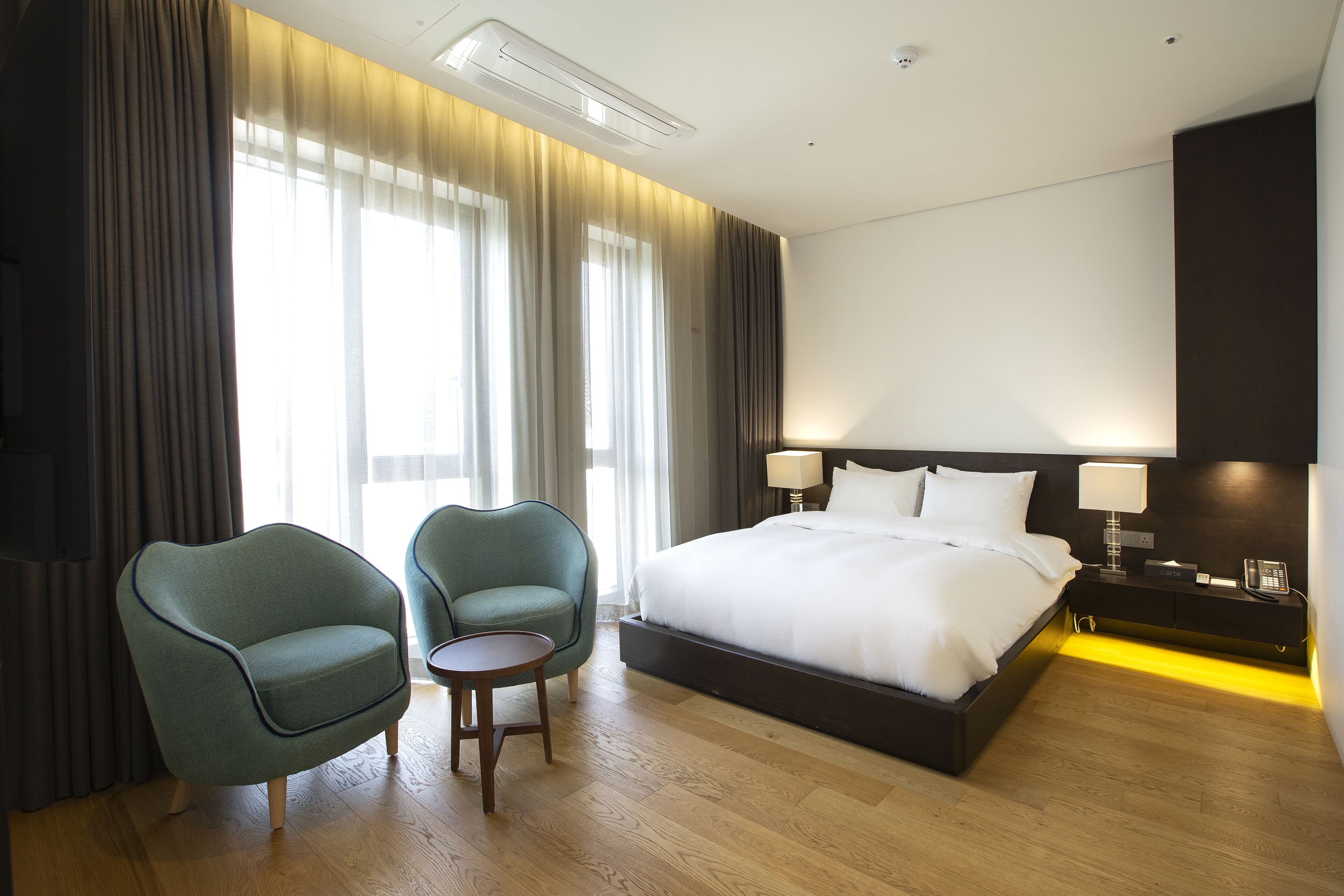 Habitación de hotel con una cama grande, dos sillones, una mesita y una mesita de noche con lámpara y teléfono.