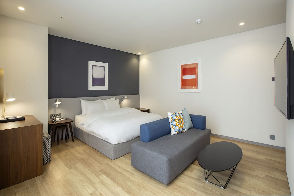 Una habitación de hotel moderna con una cama grande, un sofá, una mesita y un televisor de pantalla plana montado en la pared.